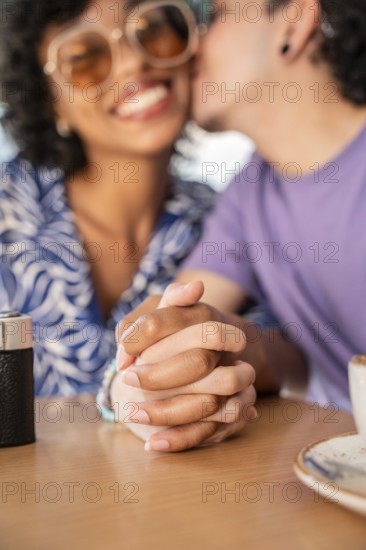 A cheerful multiethnic LGBTQ+ couple seated at a table, holding hands and sharing a tender moment,