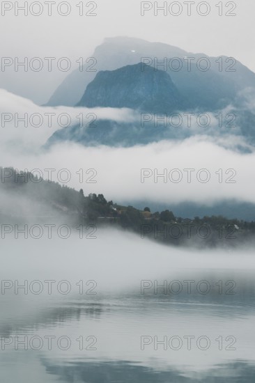 A peaceful lake reflects layers of mist and towering mountains in Norway The hazy atmosphere and