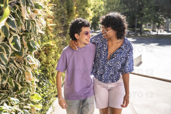 A happy, multiethnic LGBTQ+ couple walking side by side, smiling under the sunlight. Their warm