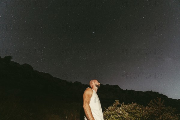 A man gazes upwards, immersed in the wonder of a star-filled night sky The serene landscape and