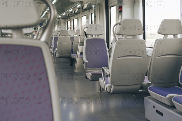 A spacious and well lit interior of a modern train, featuring rows of empty gray seats and purple.