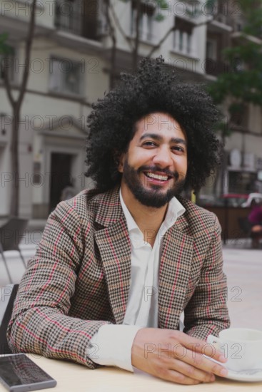 A cheerful Mixed-race man with curly hair teleworking from a street-side cafe, using a laptop and