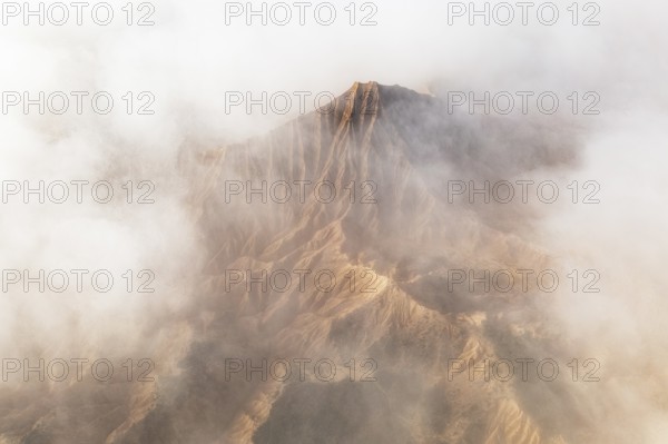 A breathtaking mountain peak emerges through a dense layer of clouds, showcasing its rugged terrain