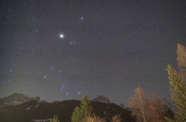 The constellations of Orion and Taurus shine brightly in the night sky, accompanied by Jupiter,