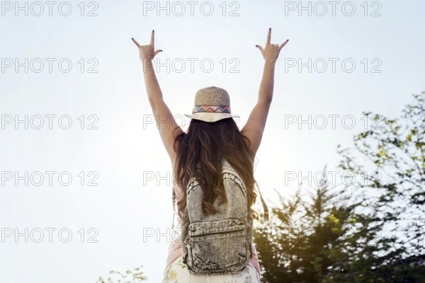 A woman wearing a hat and backpack raises her arms in a joyful sign, celebrating freedom and nature