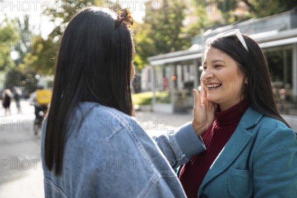 A joyful Latin lesbian couple enjoys a tender moment in a sunlit outdoor setting, expressing love