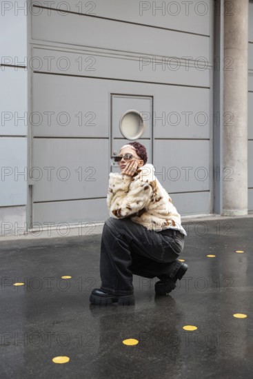 A fashionable woman wearing a fur jacket and dark jeans poses stylishly outdoors, surrounded by a