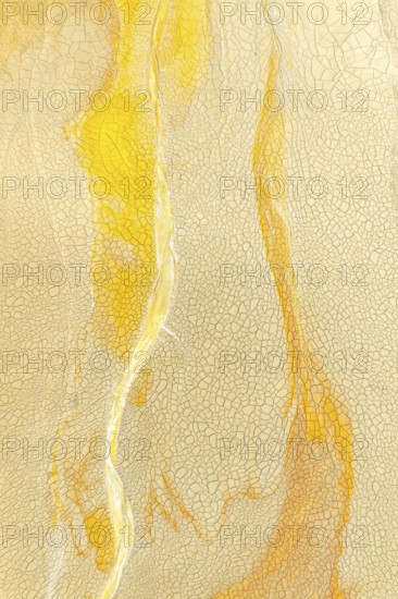 A detailed view of a cracked golden mud surface with flowing yellow lines and intricate patterns,