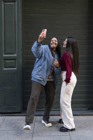 A joyful latin lesbian couple poses for a selfie in an urban setting, showcasing their unity and