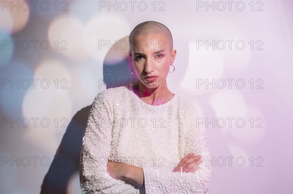 A middle-aged woman with a shaved head stands confidently against a softly lit backdrop, embodying