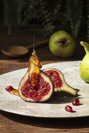 Close up of ripe figs sliced open, drizzled with golden honey. Pomegranate seeds scattered on a