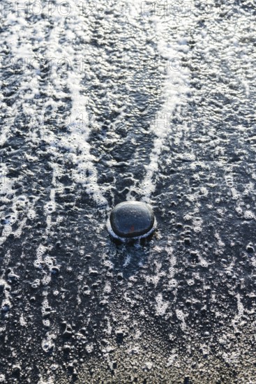 Close-up of water splash on a dark surface with bubbles and foam. The reflection adds a unique