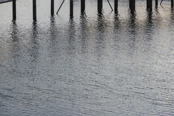 Water reflections with wooden poles standing vertically. The ripples and light reflections create a