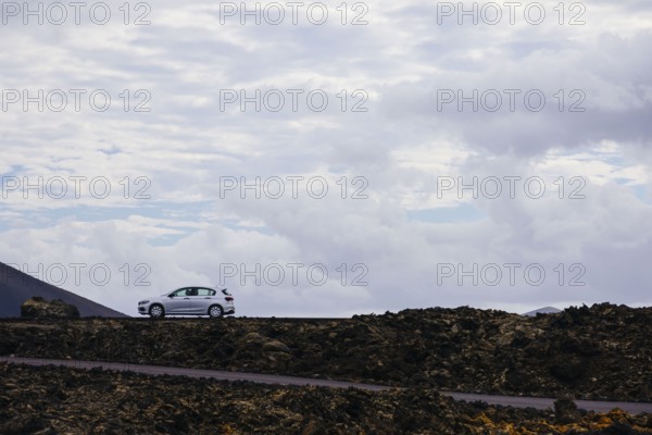 Car on a lonely road surrounded by a volcanic landscape. The rocky formations emphasize the