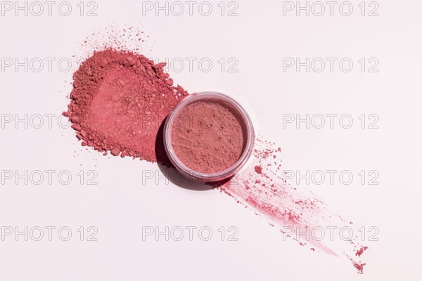 A pink blush powder elegantly spread out on a light backdrop, with an open container This image