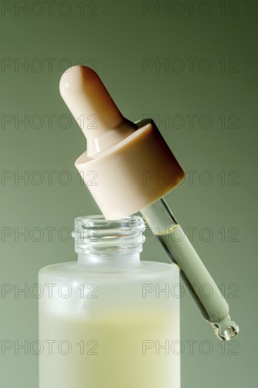 An isolated close-up of a serum dropper bottle with a droplet on a green background, perfect for
