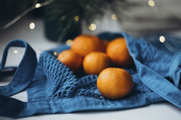 Fresh tangerines placed inside a vibrant blue string bag, set against a softly lit holiday