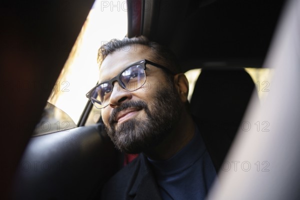 Indian businessman rides in a car on a sunny winter day, smiling warmly and looking slightly
