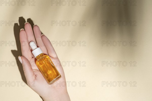 Top view of a cropped unrecognizable female hand holding a transparent dropper bottle filled with a