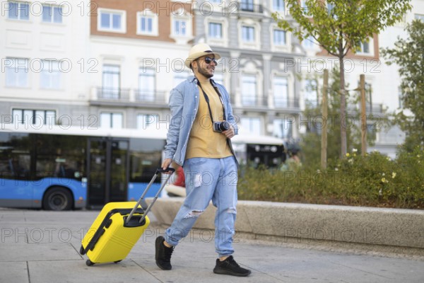 A stylish Latino transgender man strolls through the city with a camera and a vibrant yellow