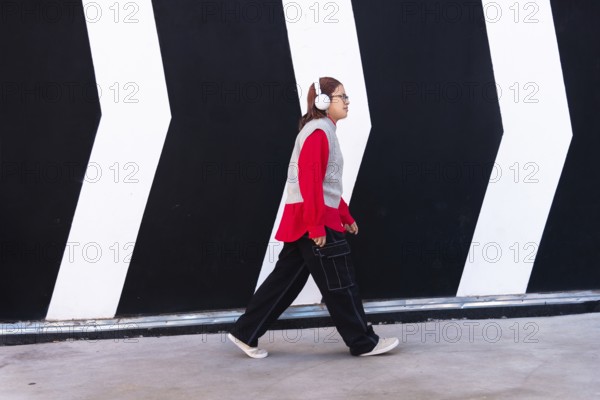 Latina woman in a vibrant red shirt and headphones walks confidently against a bold black and white