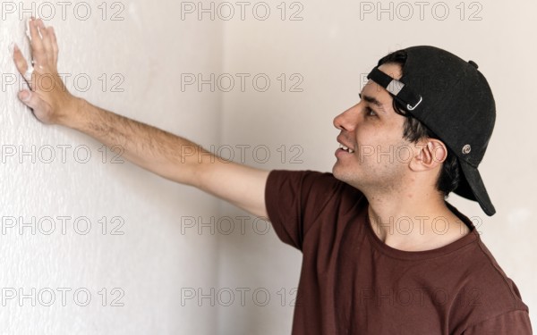 A young man inspects a wall closely during a home remodeling project, poised to begin his next task