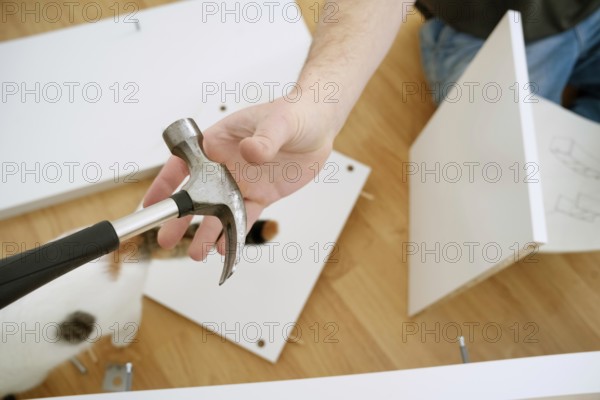 Cropped view of a man holding a hammer while assembling new furniture. The image shows his hands,