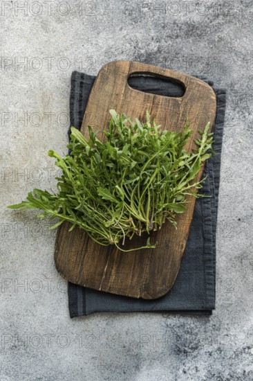 Bunch of fresh arugula placed on a rustic wooden cutting board with a dark cloth, set against a