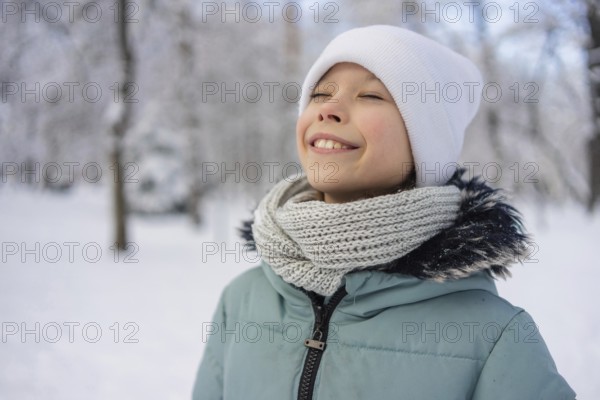 A young girl stands amidst a snowy landscape, wearing a warm scarf and hat, radiating happiness.