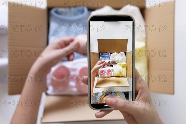 A young woman uses her smartphone to photograph clothing items for an online sale. She holds the