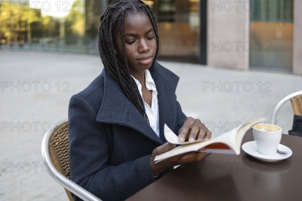An African American businesswoman with braids is sitting on an outdoor cafe table during a break,
