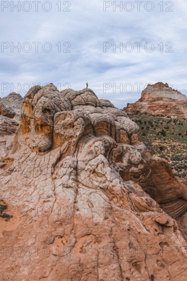 Unrecognizable explorer standing atop a unique swirling rock formation in White Pocket, Arizona,
