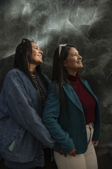 A joyful Latin lesbian couple shares a heartfelt moment, smiling warmly. They are dressed