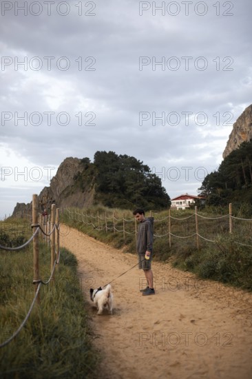 A serene scene of a man walking his dog along a sandy path in Ea, Basque Country, Spain The pathway