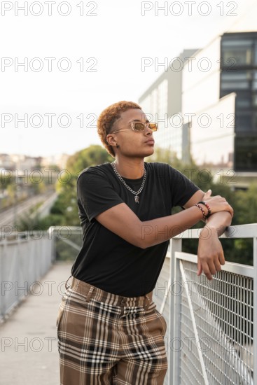Young latin transgender with short hair and sunglasses, leaning casually against a railing in an