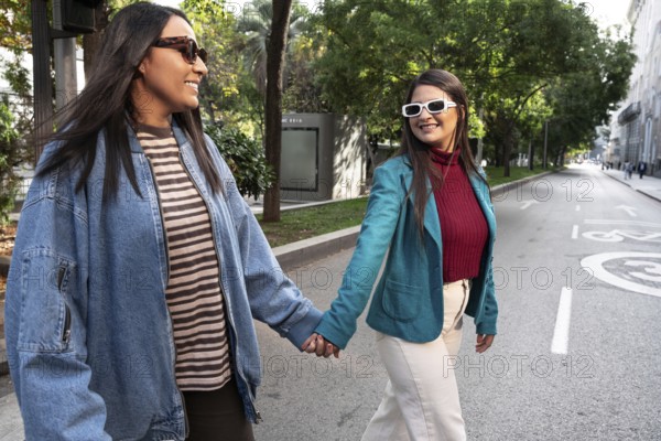 A joyful latin lesbian couple walks hand in hand down a sunlit city street, exuding happiness and