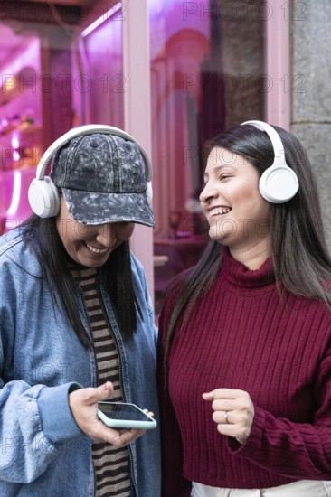 A latin lesbian couple enjoys music together with headphones. Smiling and relaxed, they share a