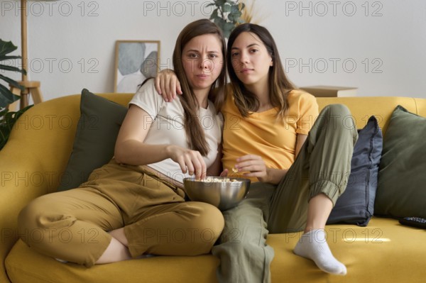 A loving lesbian couple is sitting on a comfortable sofa, enjoying a movie night with popcorn Their