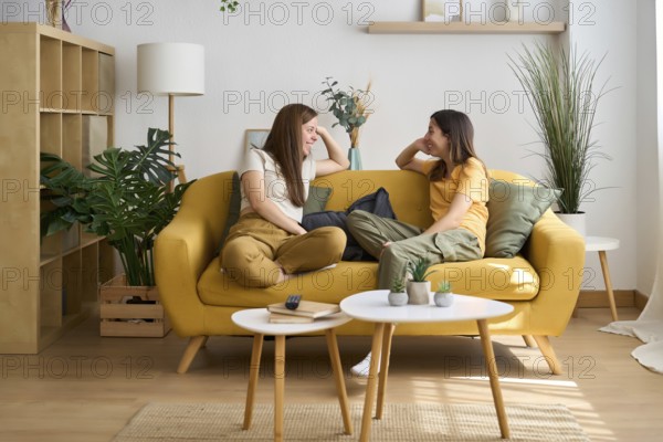 A cheerful lesbian couple enjoys a cozy moment on a yellow sofa The room is filled with greenery