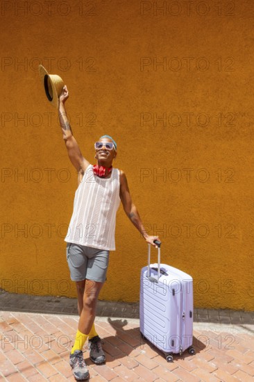 LGBTQIA+ man joyfully preparing for a holiday, standing with a suitcase against a vibrant orange