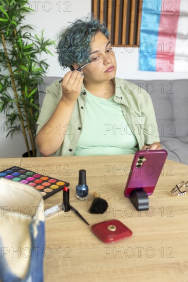 A transgender man meticulously applies makeup while recording a tutorial with his mobile phone.