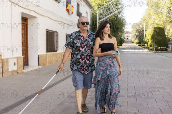 A blind father, utilizing a white cane, walks confidently through a town, guided by his attentive