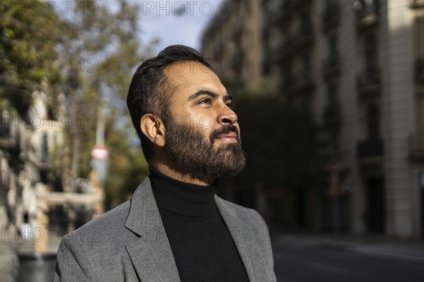 A confident Indian man dressed in a business-appropriate gray coat and black turtleneck is captured