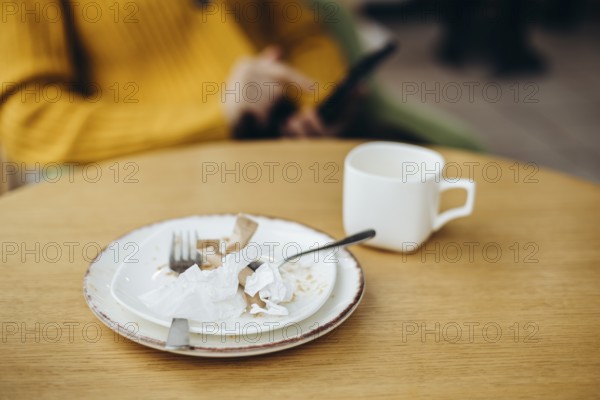 A cozy coffee shop setting featuring a wooden table with a used cup and plate Crumpled paper