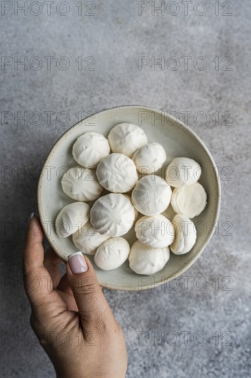 A hand holding a small ceramic bowl filled with handmade mini zephyr marshmallows, highlighting