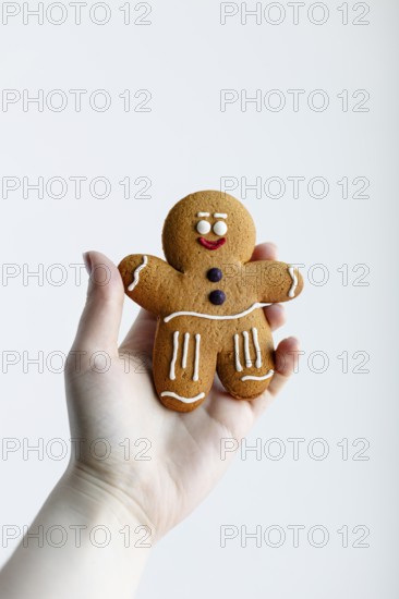 A hand holding a cheerful gingerbread man cookie, decorated with white and red icing, isolated