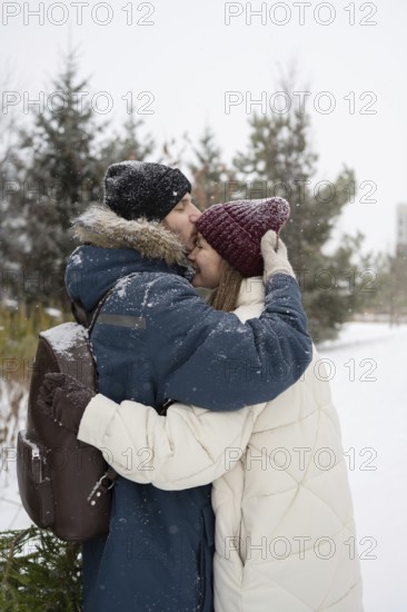 A man lovingly kisses a woman on the forehead as they embrace in a snowy park Dressed in winter