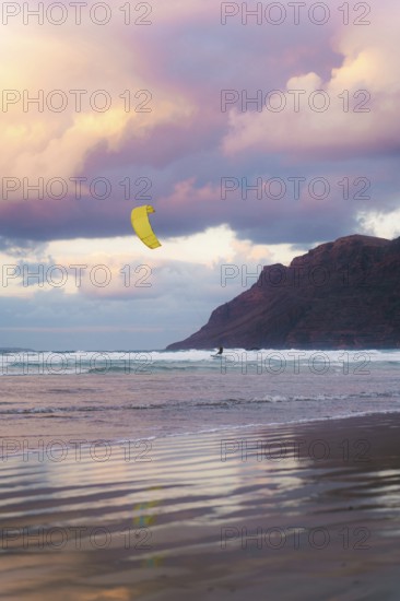 A kite surfer glides across the waves at Famara Beach, Lanzarote, under a sky painted with stunning