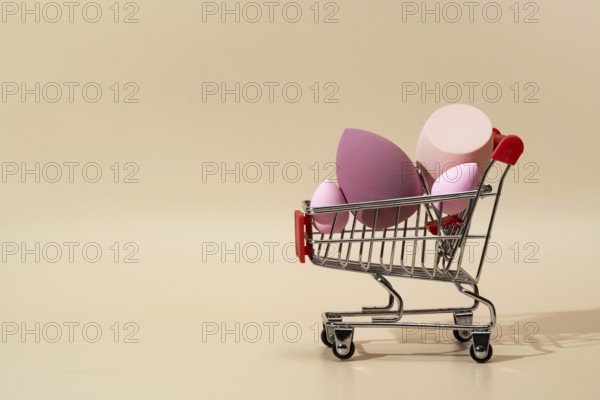 A collection of vibrant cosmetic sponges displayed in a miniature shopping cart against a soft