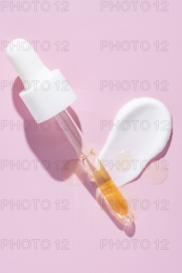 A dropper dispenses golden serum beside a white cream smear on a vibrant pink surface, representing
